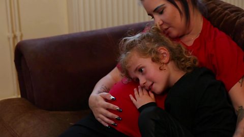 A young girl resting her head on her mum's baby bump.