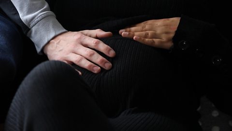 A close up of a mum's bump with her and her partner's hand upon it.