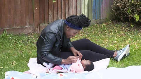 A mum raising her daughter's arms gently while she lies with her back on a mat.