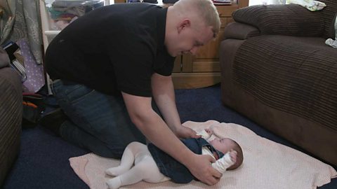 A dad making eye contact with his baby daughter lying on her back on a mat.