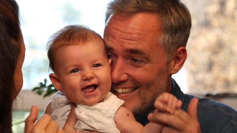 A dad holding his smiling baby daughter close to his face as they dance.