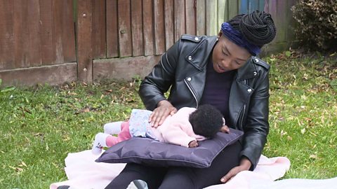 A mum talking to her baby on a cushion and rubbing her back.