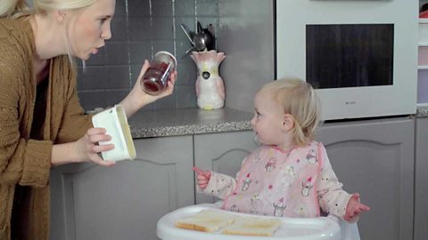 A mum offering her little girl a choice of butter or jam for her toast.