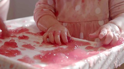 A baby girl's hands in a lot of jelly.