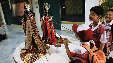 A group of boys play with two elaborate rod puppets, controlling each hand separately with a different rod.