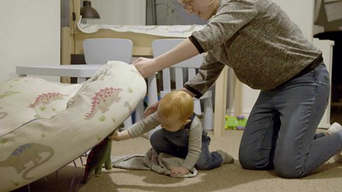 A little boy hiding a dinosaur toy under a cushion.