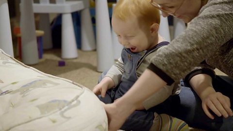 A little boy laughing as his mum lifts the cushion to reveal his toy.