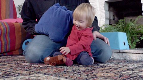 A little girl excitedly picking up a monkey toy from under a cushion.