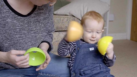 A little boy clapping two cups together.