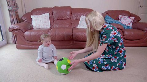 A mum rolling a soft football toy to her little girl in their living room.