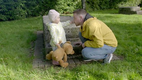 A little girl pointing to her dad's nose.