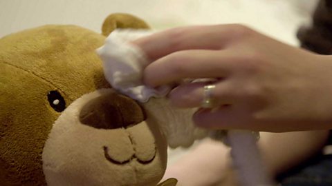 A mum's hand sponging a teddy's eye with a cloth.