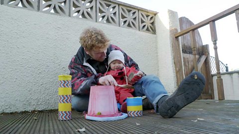 A big brother and his toddler sister banging buckets with a wooden spoon.