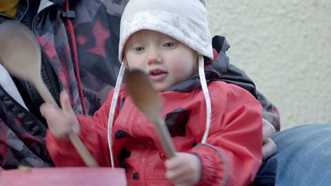 A little girl hitting a bucket with wooden spoons.