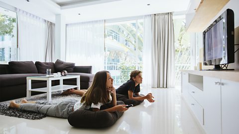 Two people lay on the floor in a bright room watching television.