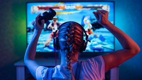 A person cheers with a game controller in their hand as they play a fighting video game.