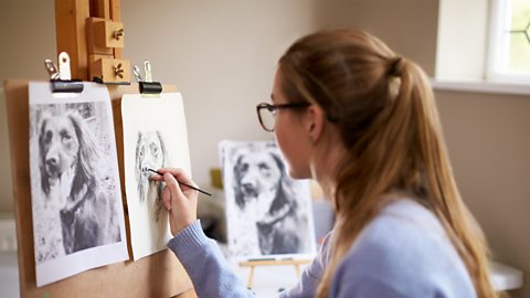 A person draws dog portraits in a bright room against an easel. 