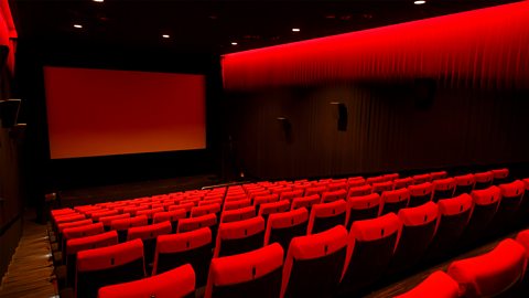 A photo of a cinema screen with rows of red seats.