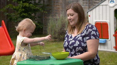 Toddler playing with spaghetti in soil with mum in the garden. 