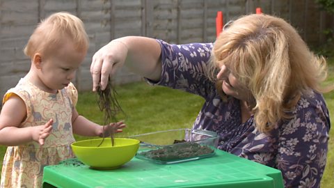 Mum playing with spaghetti in soil with her daughter in the garden. 