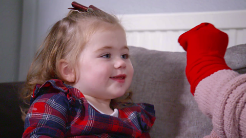 Toddler sat on sofa and looking at red hand puppet