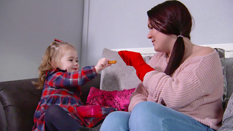 Toddler sat on sofa with mum feeding food to a red sock puppet