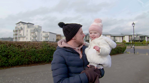 Man in bobble hat holds his toddler daughter who is also wearing a bobble hat