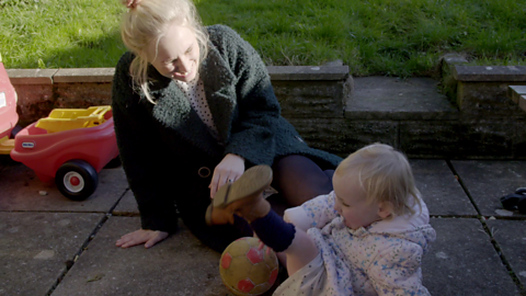 Woman and toddler sat on garden patio playing with ball