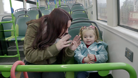 Woman sat on bus seat with toddler and clapping