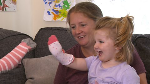 Little girl playing sock puppets on the sofa.