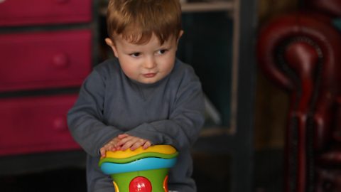 Little boy banging on toy drum.