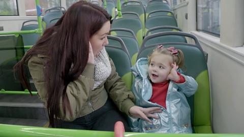 Mum and her little girl on a bus both holding hands to their ears