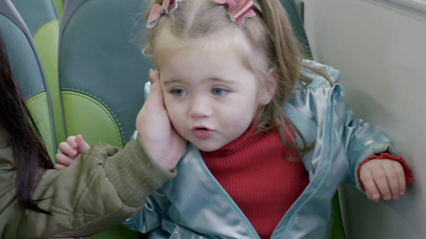 Toddler on bus talking while her mum places her hand on her ear