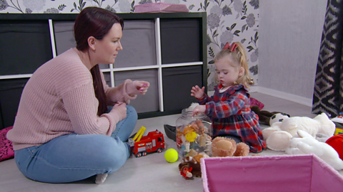 Woman and toddler sat on floor tidying toys