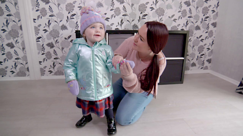 Woman kneeling on floor and placing glove on hand of toddler