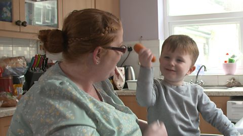 Little boy holding up a carrot and showing his mum in the kitchen. 