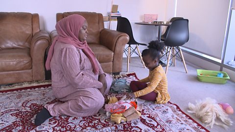 Mum and daughter sat on living room floor, looking at a pile of laundry. 