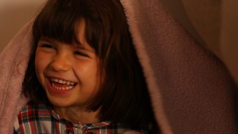 Little girl smiling with a blanket on her head. 