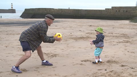 Little boy and granddad throwing a ball on the beach.