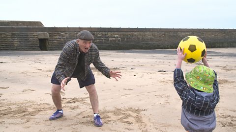 Granddad on the beach ready to catch a ball, thrown by little boy. 