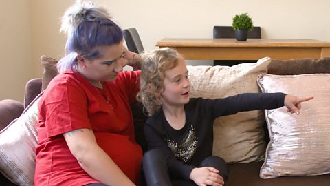 Mum and daughter sat on sofa, pointing to the right.