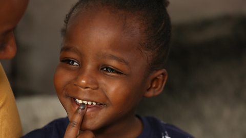 Little boy smiling with a finger on his mouth.