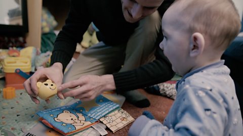 Baby looking at a bear toy and a picture book. 