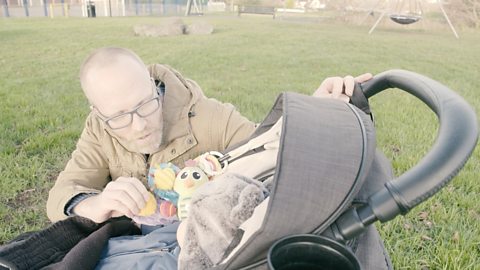 Dad looking at baby in pram at the park. 