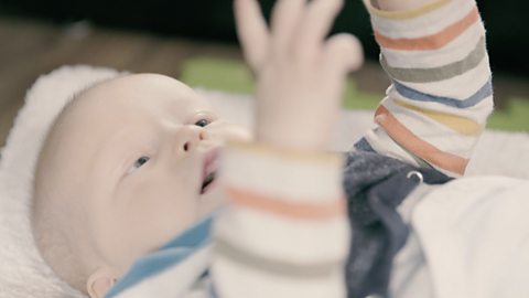 Baby lying down and smiling, arms reaching up.