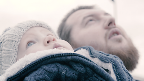 Dad and baby with hat looking up at sky.