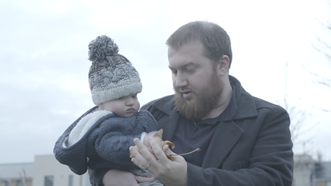 Dad holding baby, showing him a leaf.