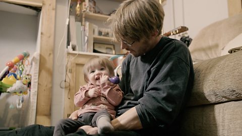 Dad holding baby with rattle in her mouth.