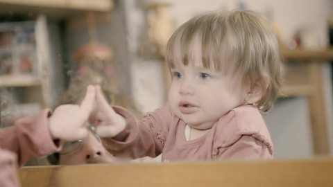 Baby looking in a mirror with hands up.