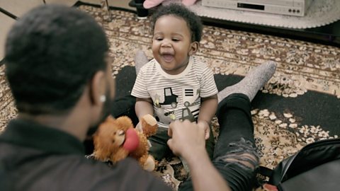 Dad facing smiling baby, both sat on the floor.